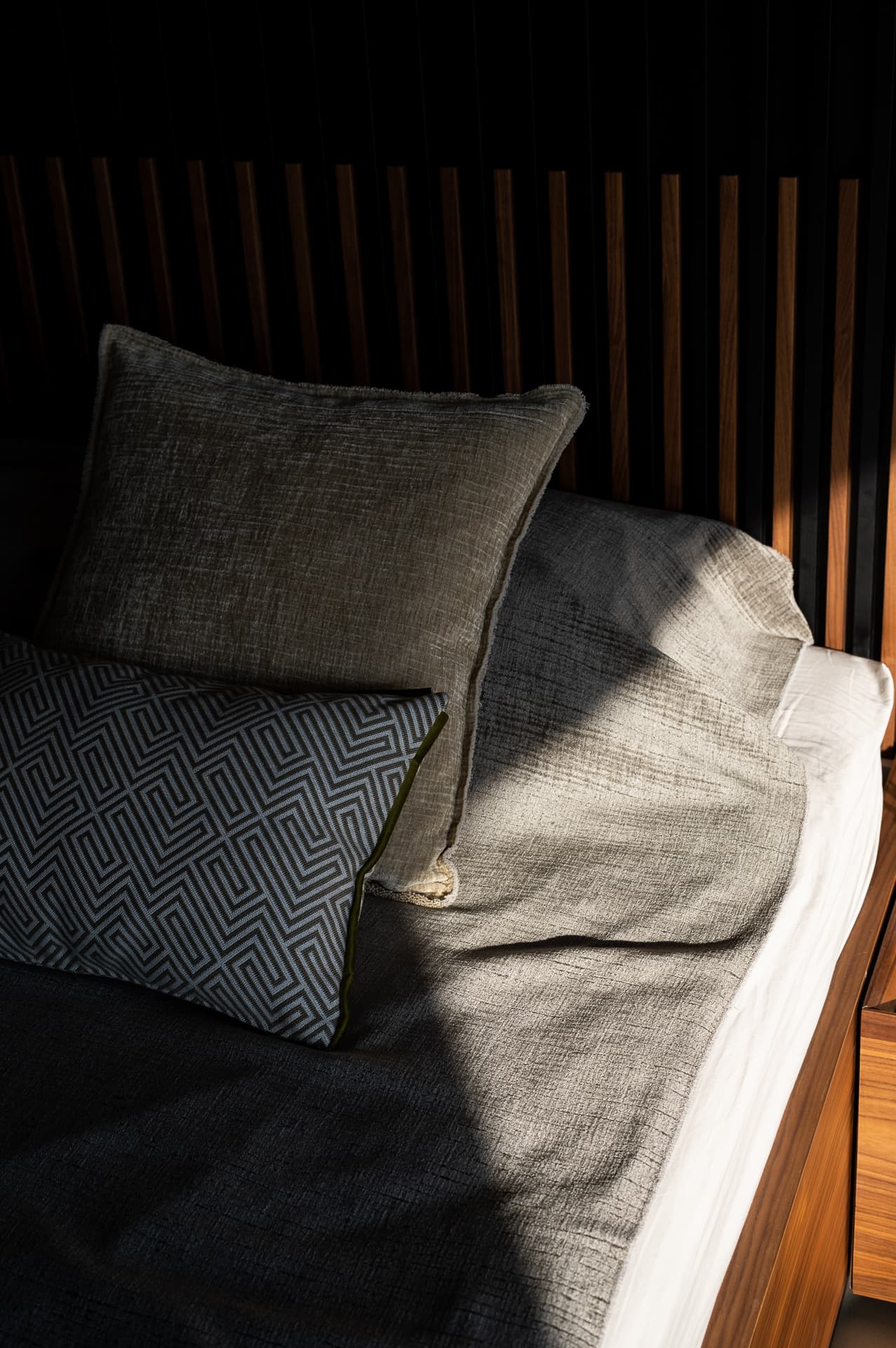 Textured linen cushions with a geometric pattern on the walnut bed in raking light in the master bedroom of Timeless Union