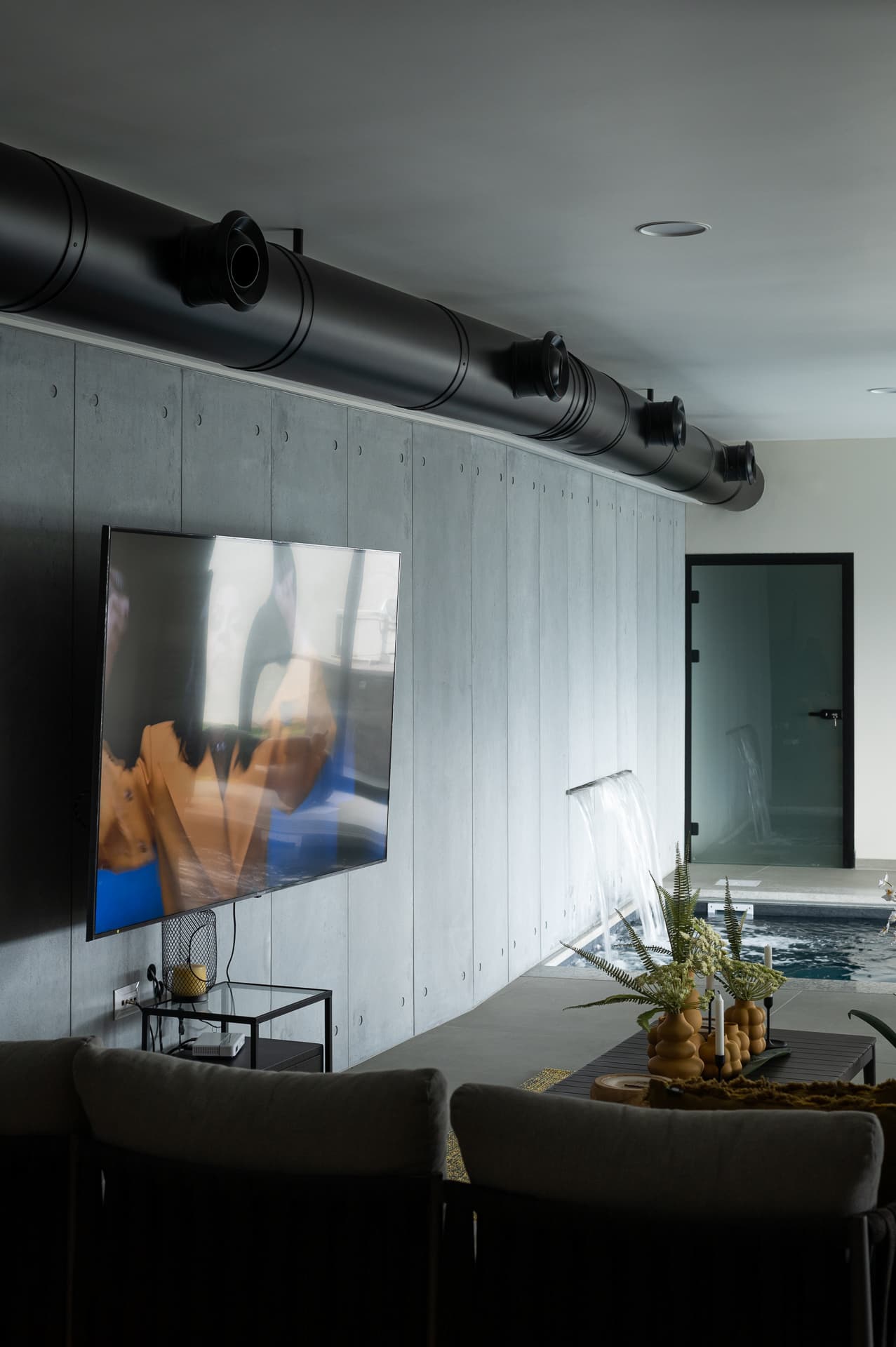 Lounge beside the indoor pool with a concrete wall, exposed black ductwork and a wall-mounted screen in Timeless Union