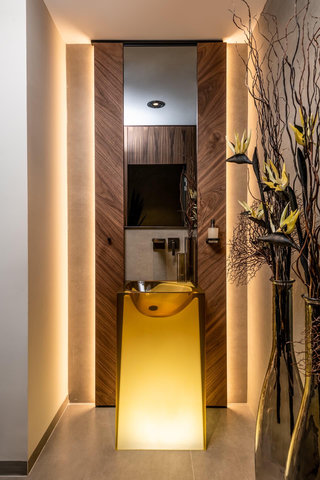 Glowing amber glass pedestal basin in a narrow powder room lined with walnut and soft cove lighting in Timeless Union
