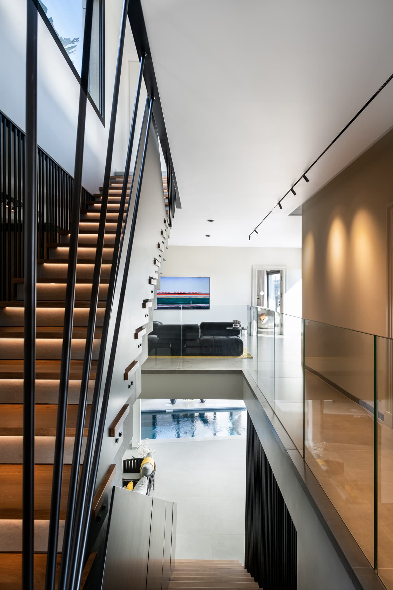 Stair with backlit oak treads and slender black rods overlooking a glass-railed gallery and the pool below in Timeless Union