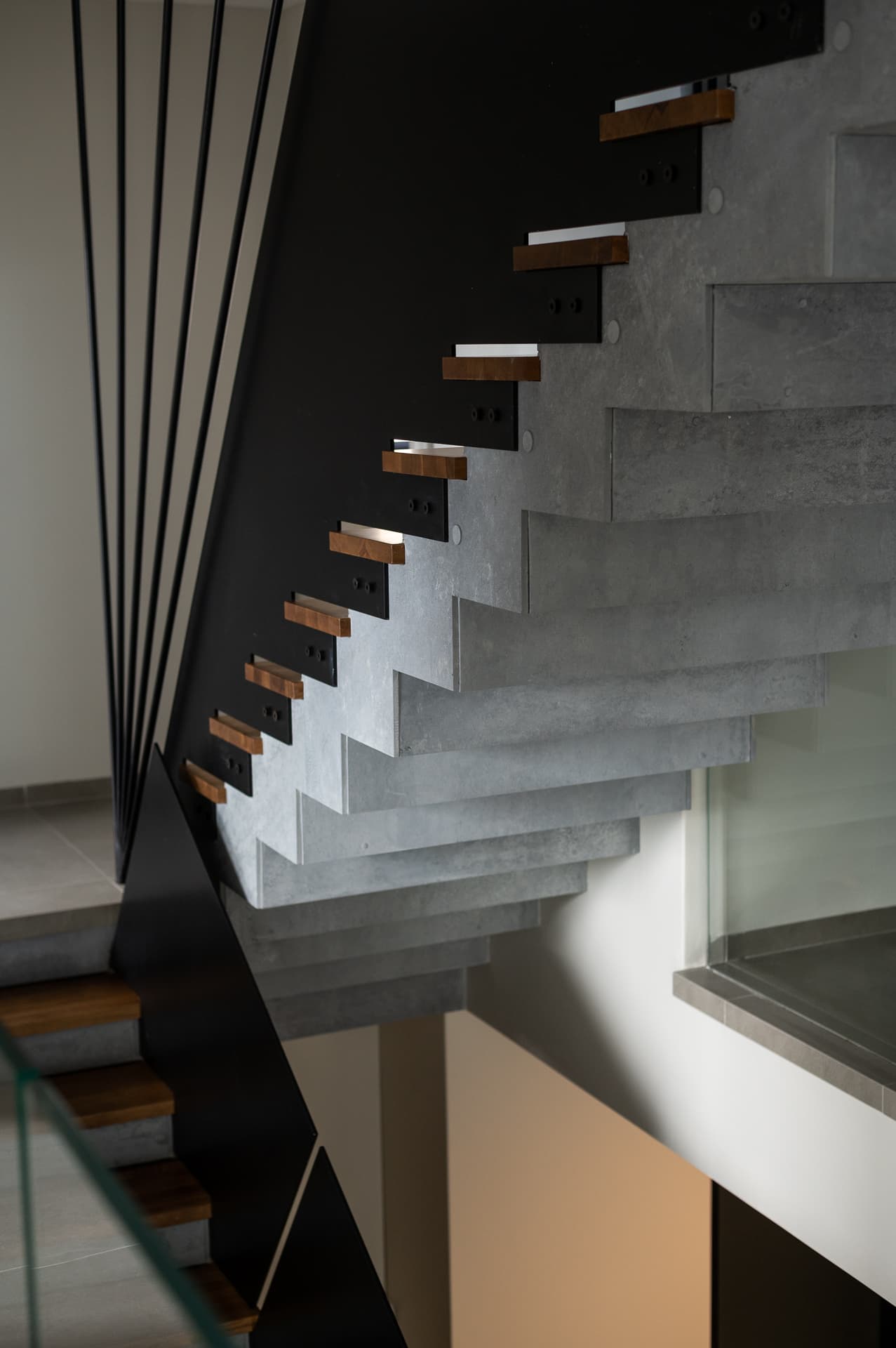 Underside of a cantilevered concrete stair with oak tread ends and black steel stringer in Timeless Union