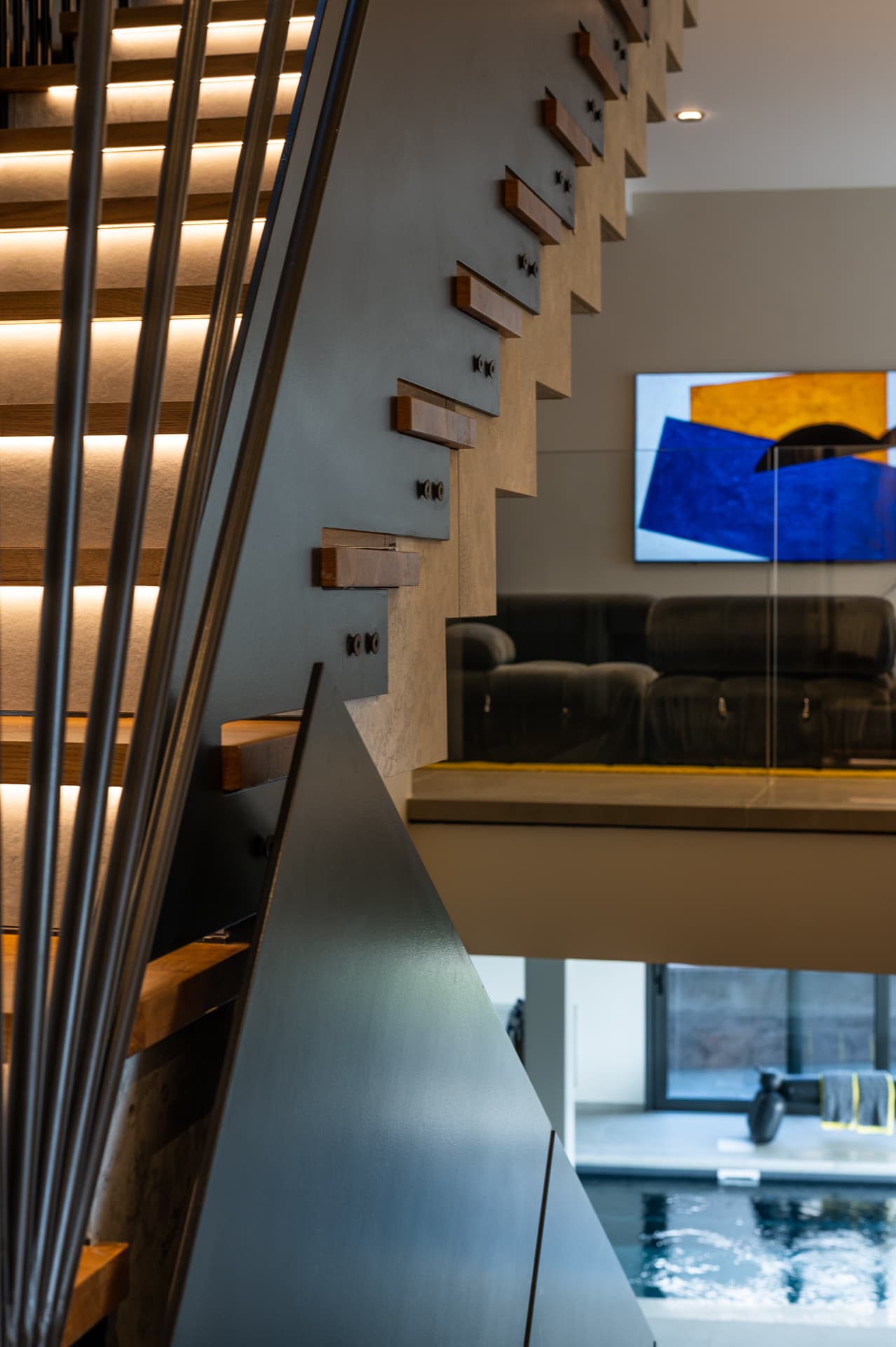 Backlit stair treads and a black steel wedge rail seen beside the gallery lounge and pool below in Timeless Union