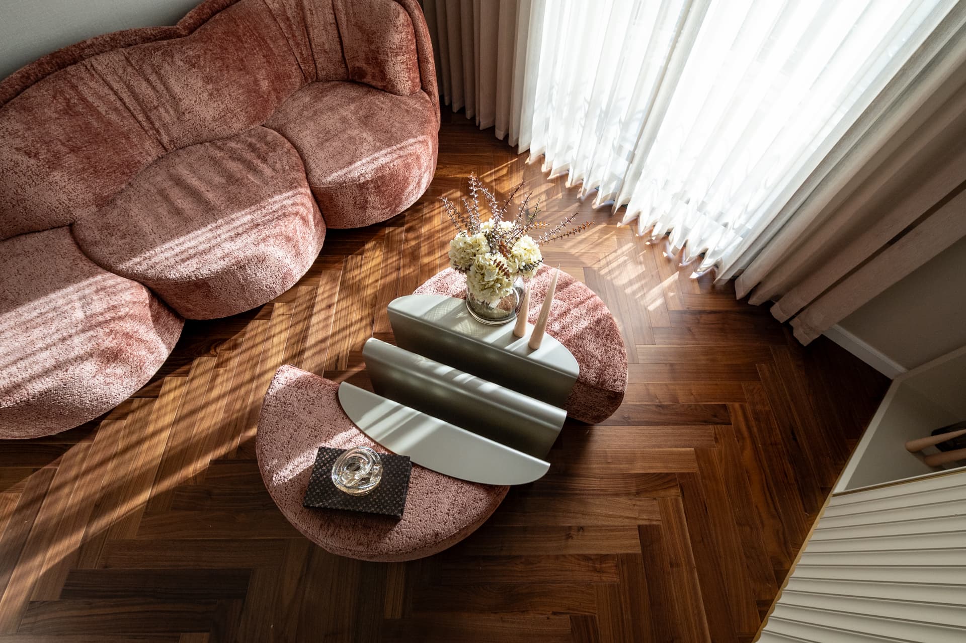Overhead view of a scalloped blush velvet sofa and split-level coffee tables on herringbone walnut floor in the second bedroom of Twilight