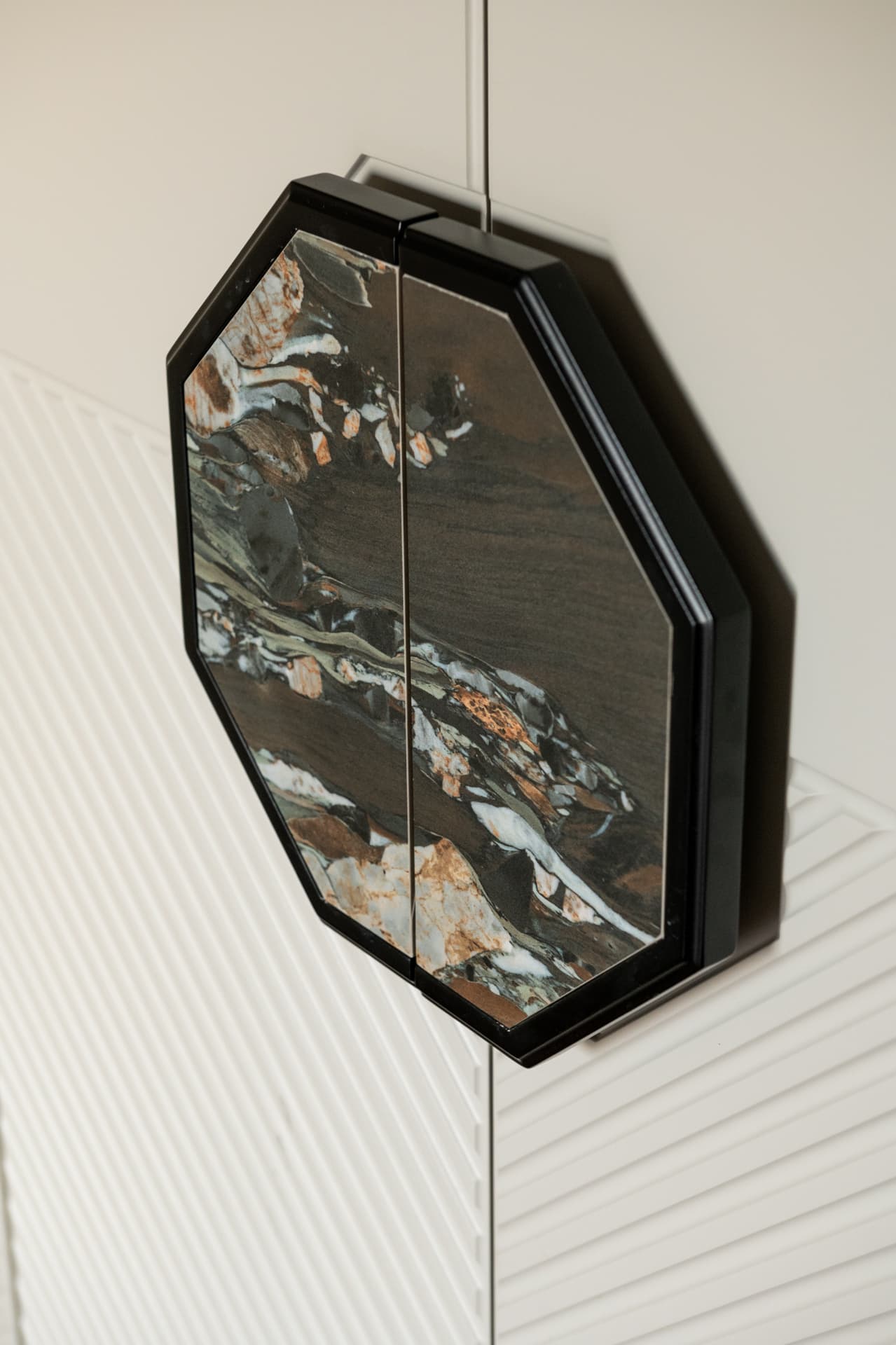 Octagonal cabinet pull faced in dark veined stone on a white door with diagonal grooved panels in the third bedroom of Twilight