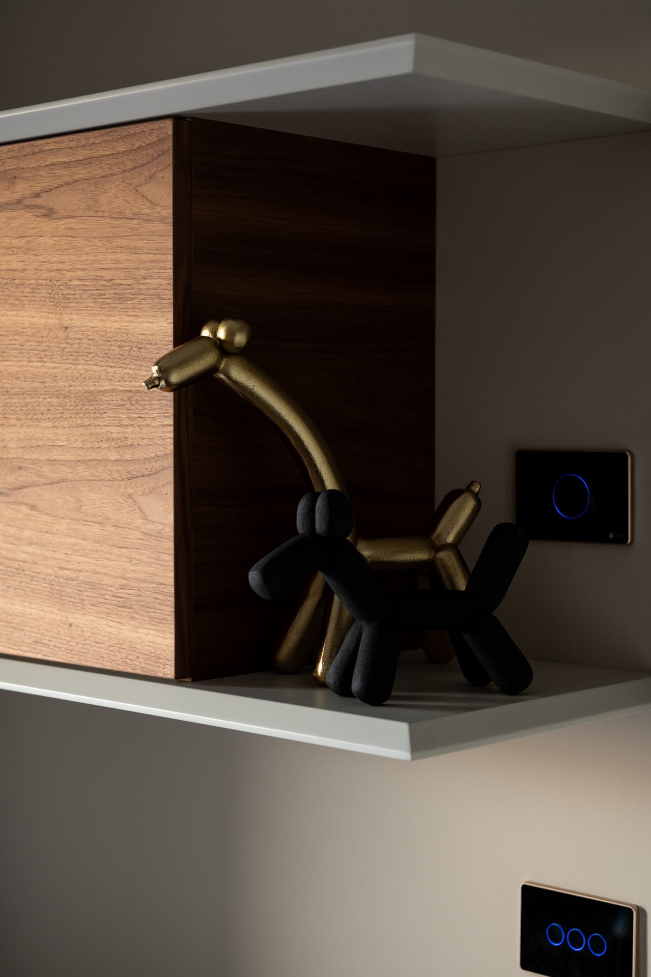 Brass and black balloon-animal figurines on a white shelf with a walnut cabinet box and touch switches in the third bedroom of Twilight