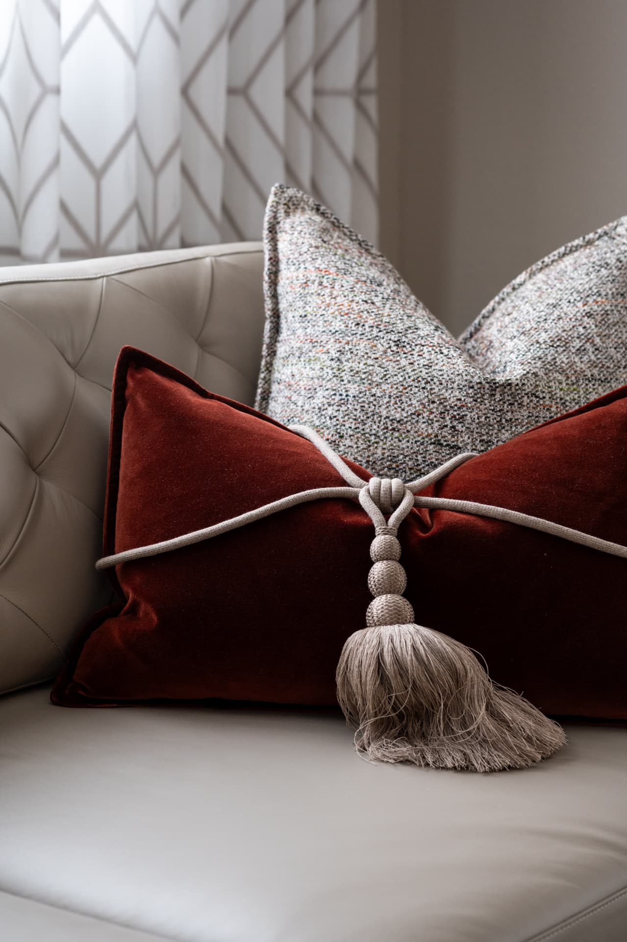 Rust velvet cushion bound with a corded tassel against a tweed cushion on an ivory tufted leather sofa, a textile detail from Twilight