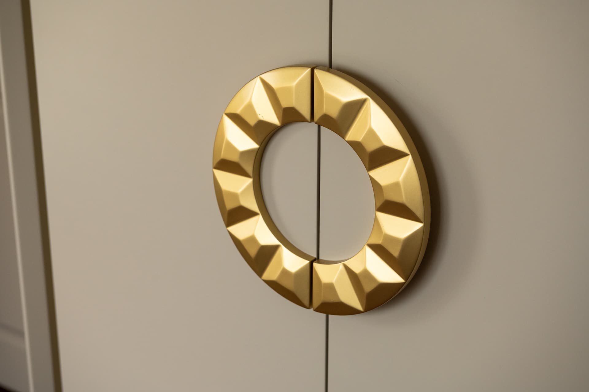 Faceted brass ring pull split across two cream lacquered cabinet doors, a hardware detail from Twilight