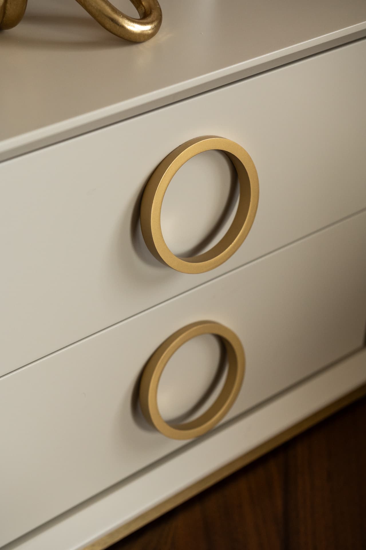 Slim brass ring pulls on a pair of cream lacquered drawers above a walnut floor, a hardware detail from Twilight