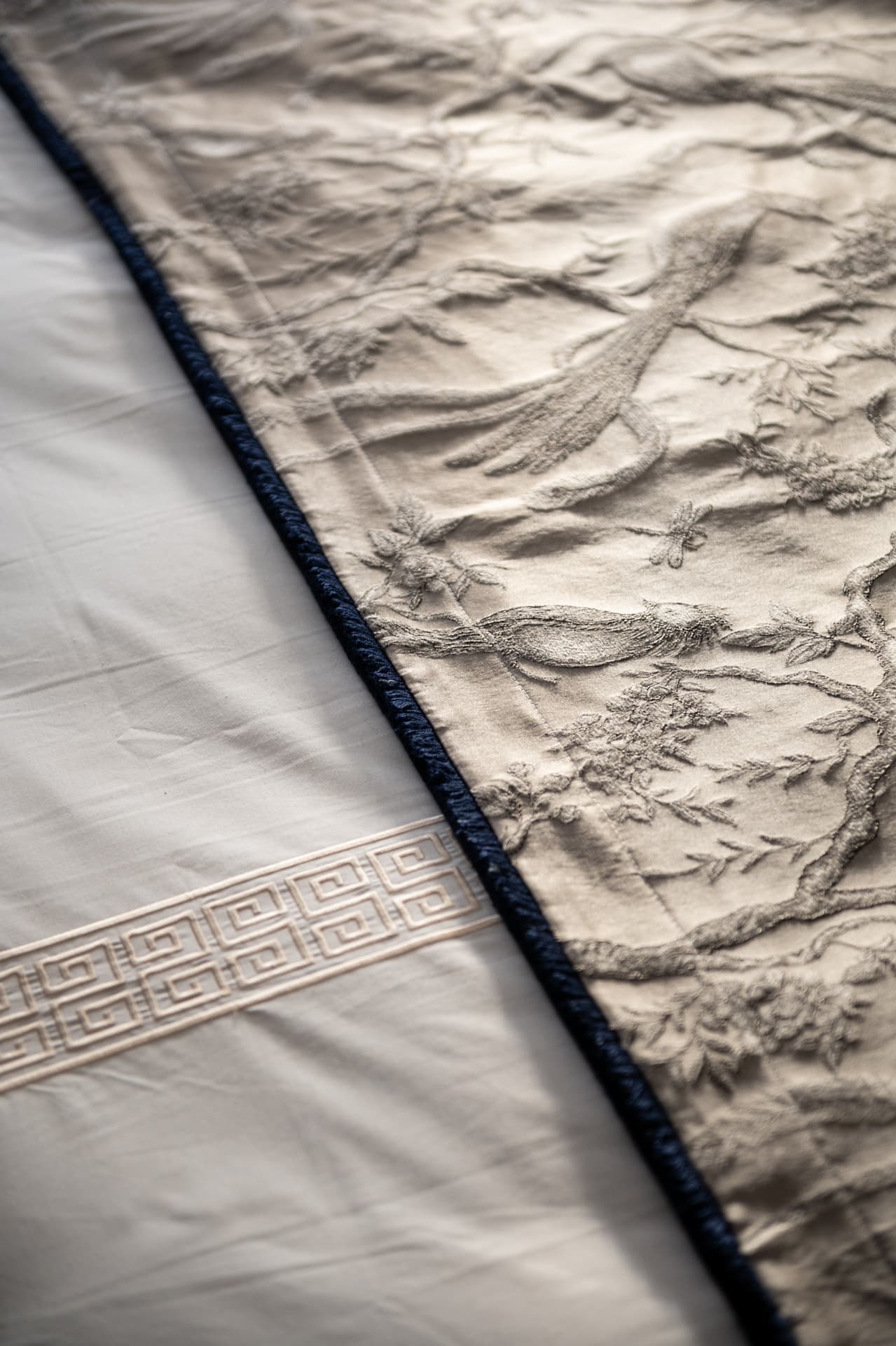 Bird-and-branch embroidered bed runner with navy cord trim over white linen with a Greek key band in the master bedroom of Twilight
