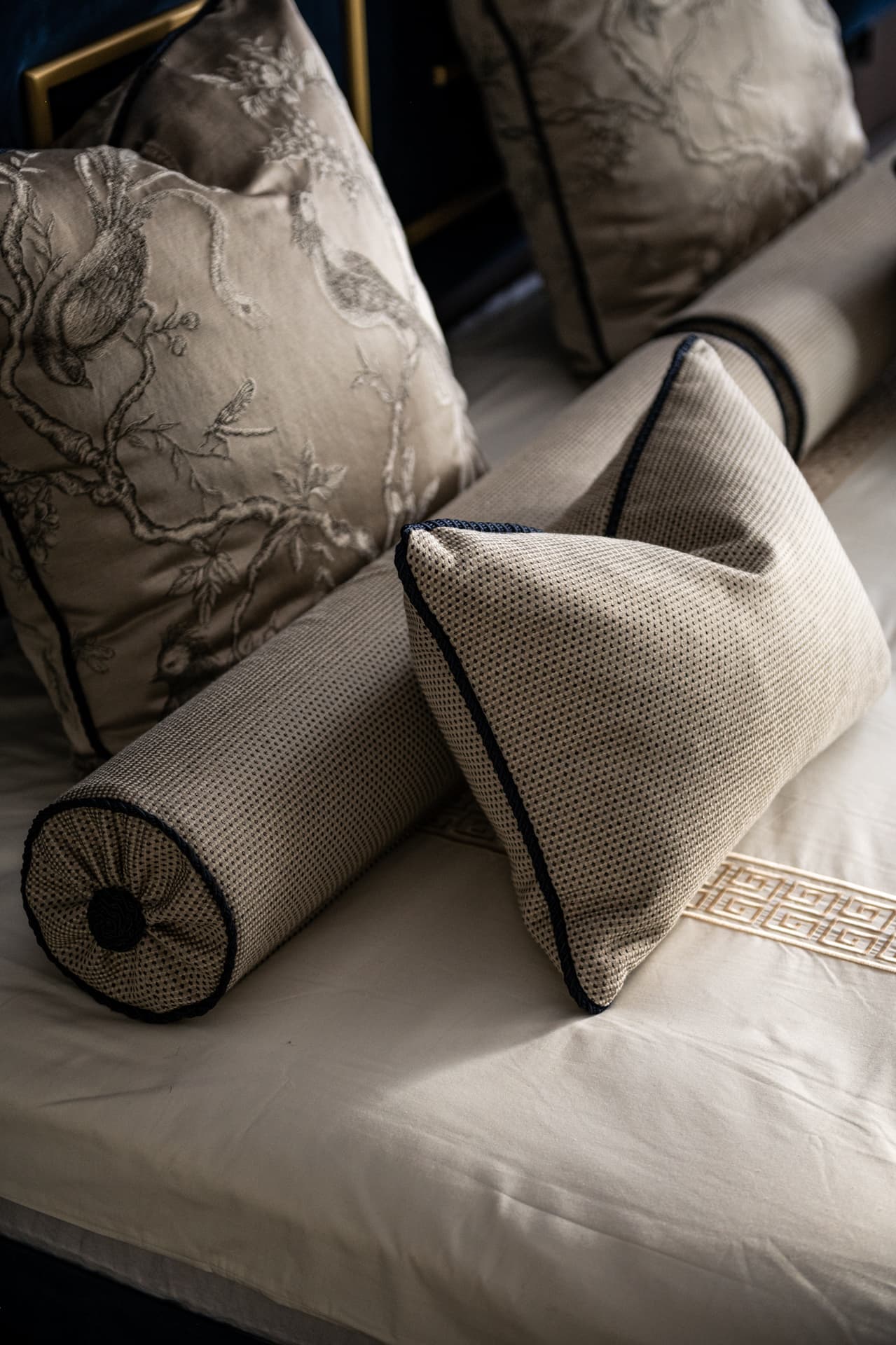 Close view of piped dotted bolsters and bird-embroidered cushions on Greek key bed linen in the master bedroom of Twilight