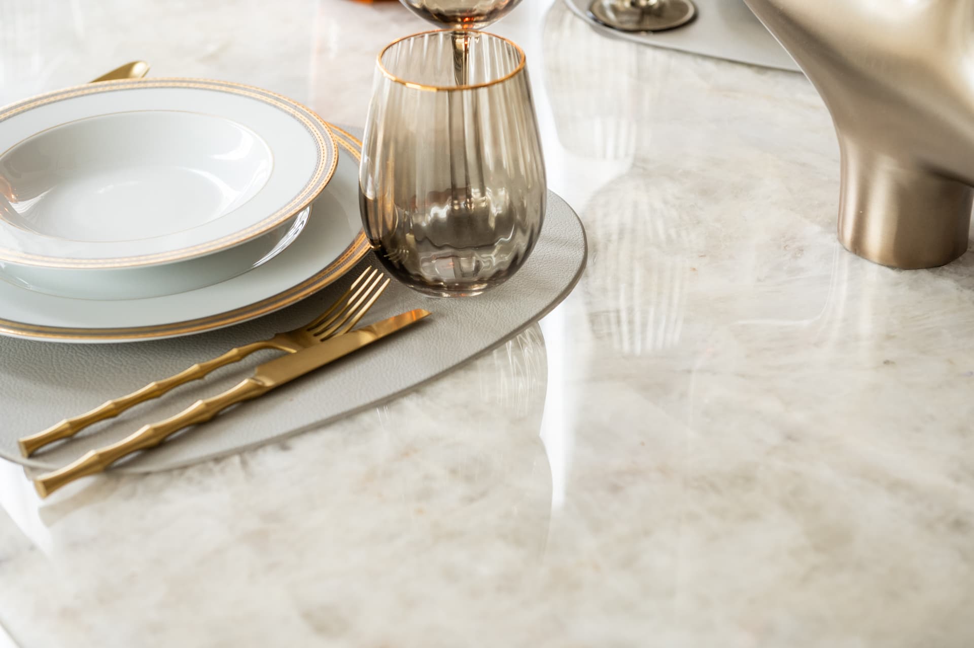 Gold-rimmed plates and a smoked tumbler beside a sculptural metal centrepiece on a glossy stone table in the dining room of Twilight