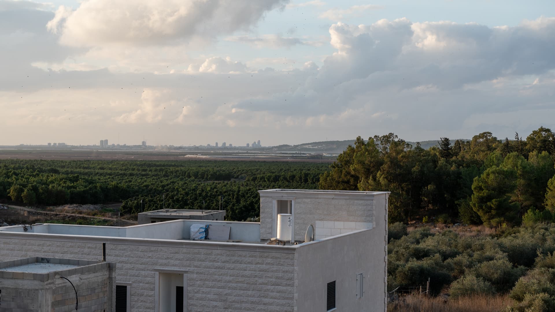View from Twilight over neighbouring stone-clad houses, orchards and pine trees toward a distant skyline under evening clouds