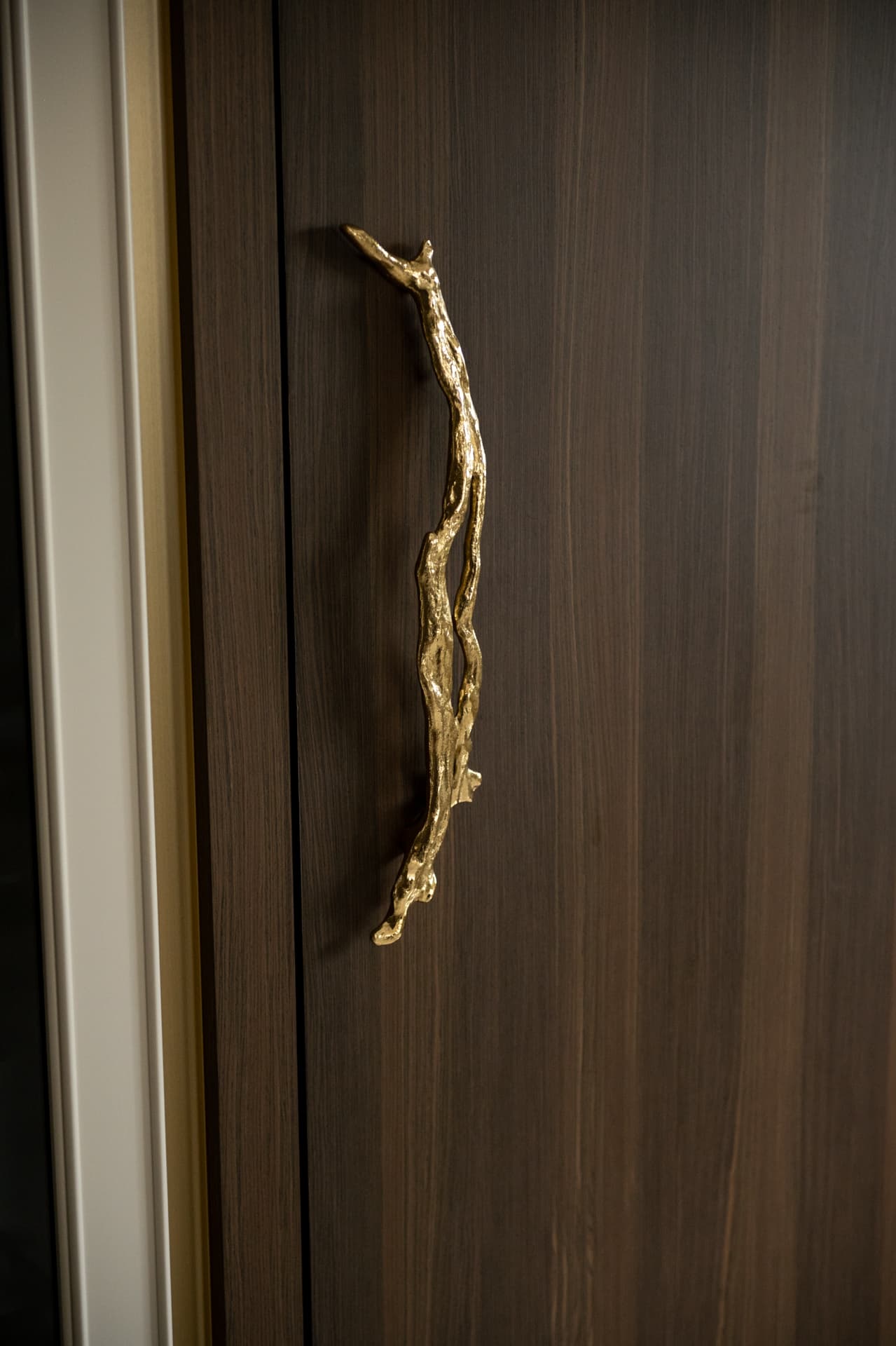 Brass branch-shaped pull on a tall dark wood cabinet door with a cream painted frame in the kitchen of Twilight