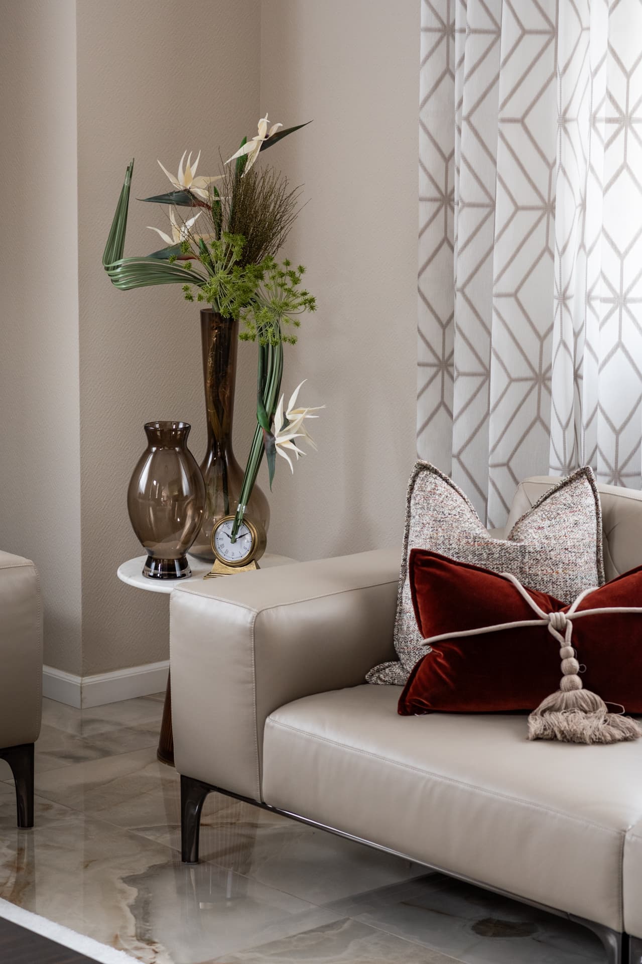 Ivory leather sofa with a velvet tasselled cushion beside amber glass vases and a lattice sheer curtain in the living room of Twilight