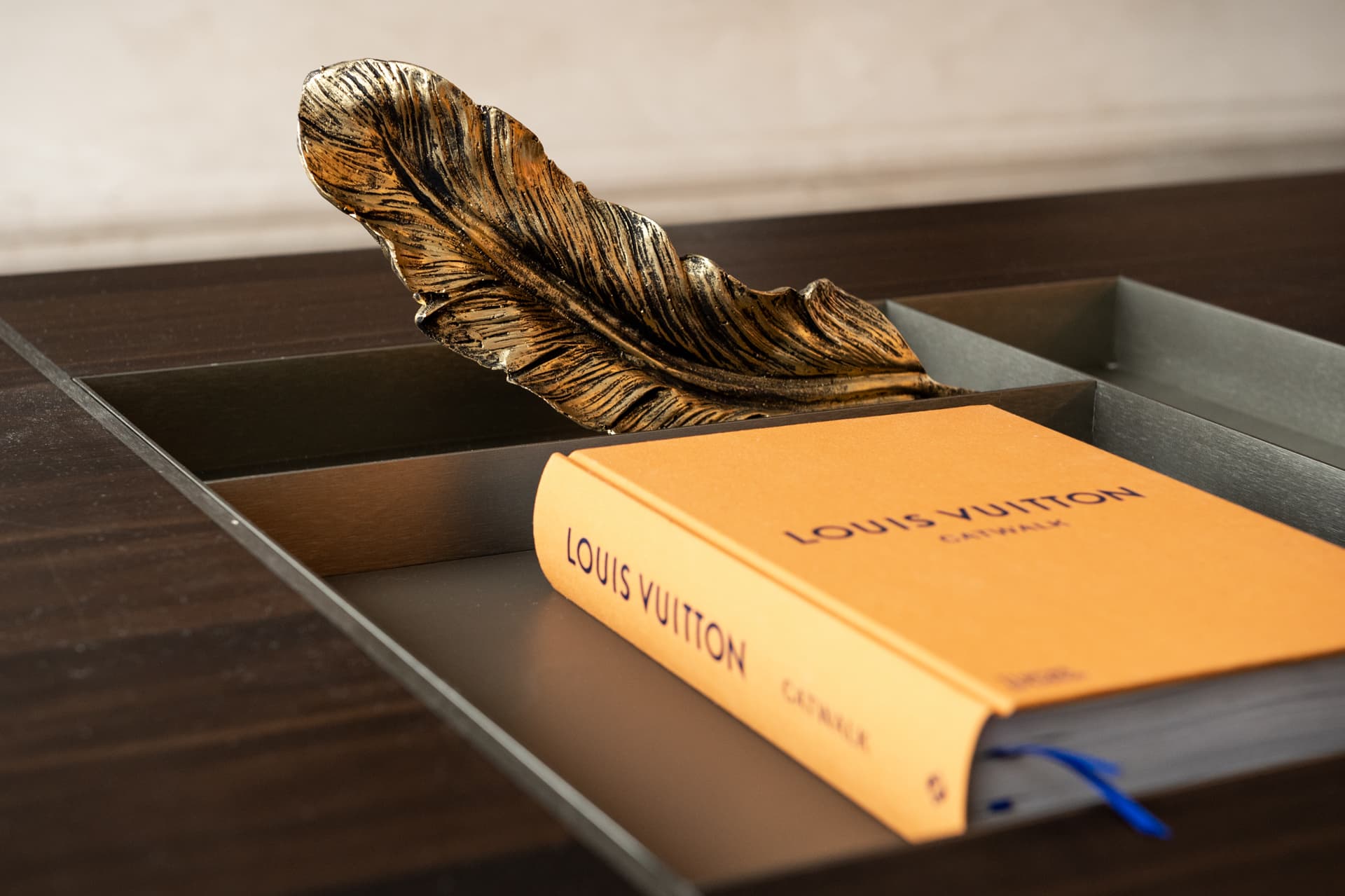 Gilded feather sculpture and a coffee table book in the recessed metal tray of a dark wood coffee table in the living room of Twilight