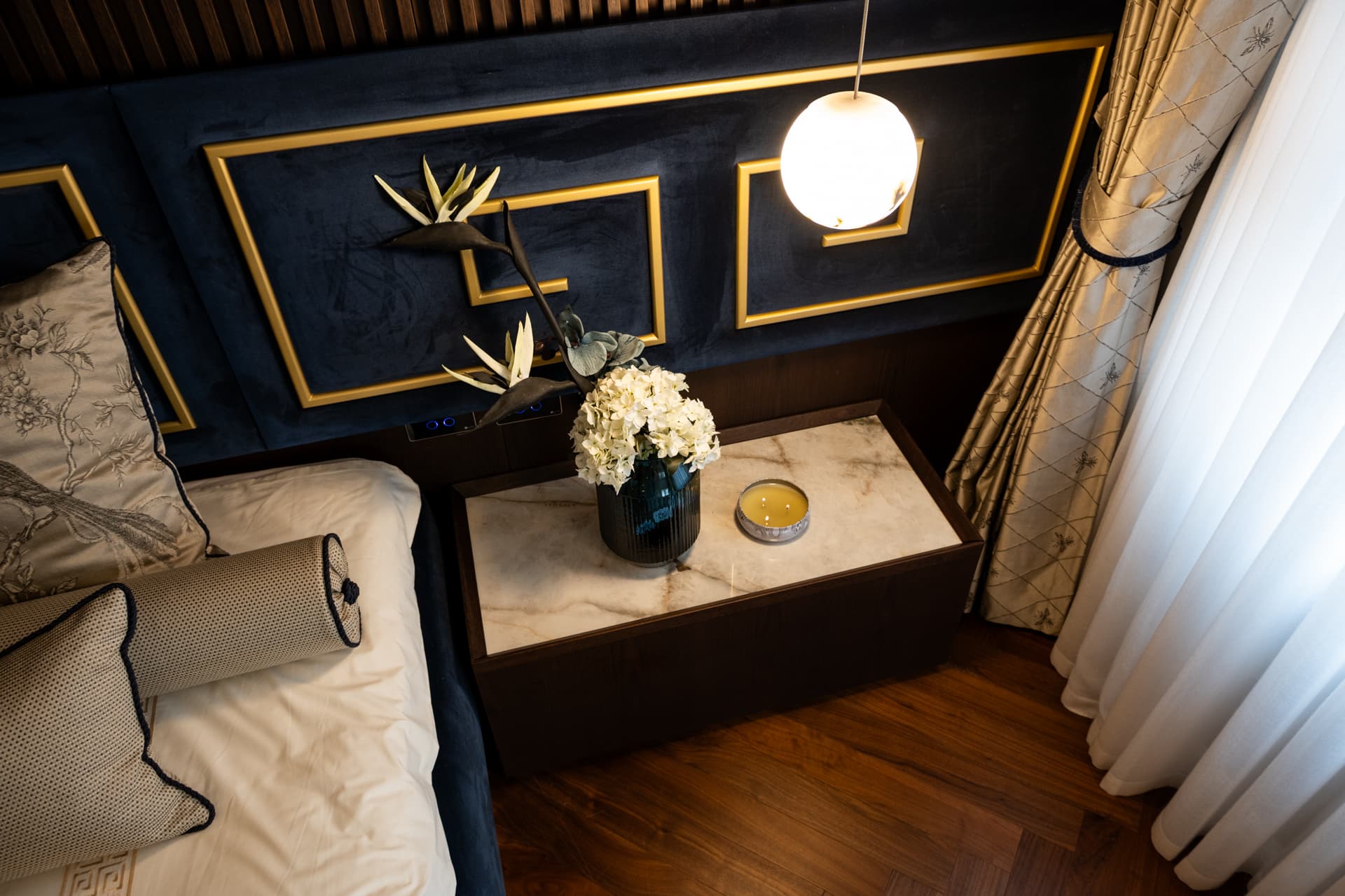 Overhead view of a stone-topped nightstand under a navy velvet headboard with brass fret inlays in the master bedroom of Twilight