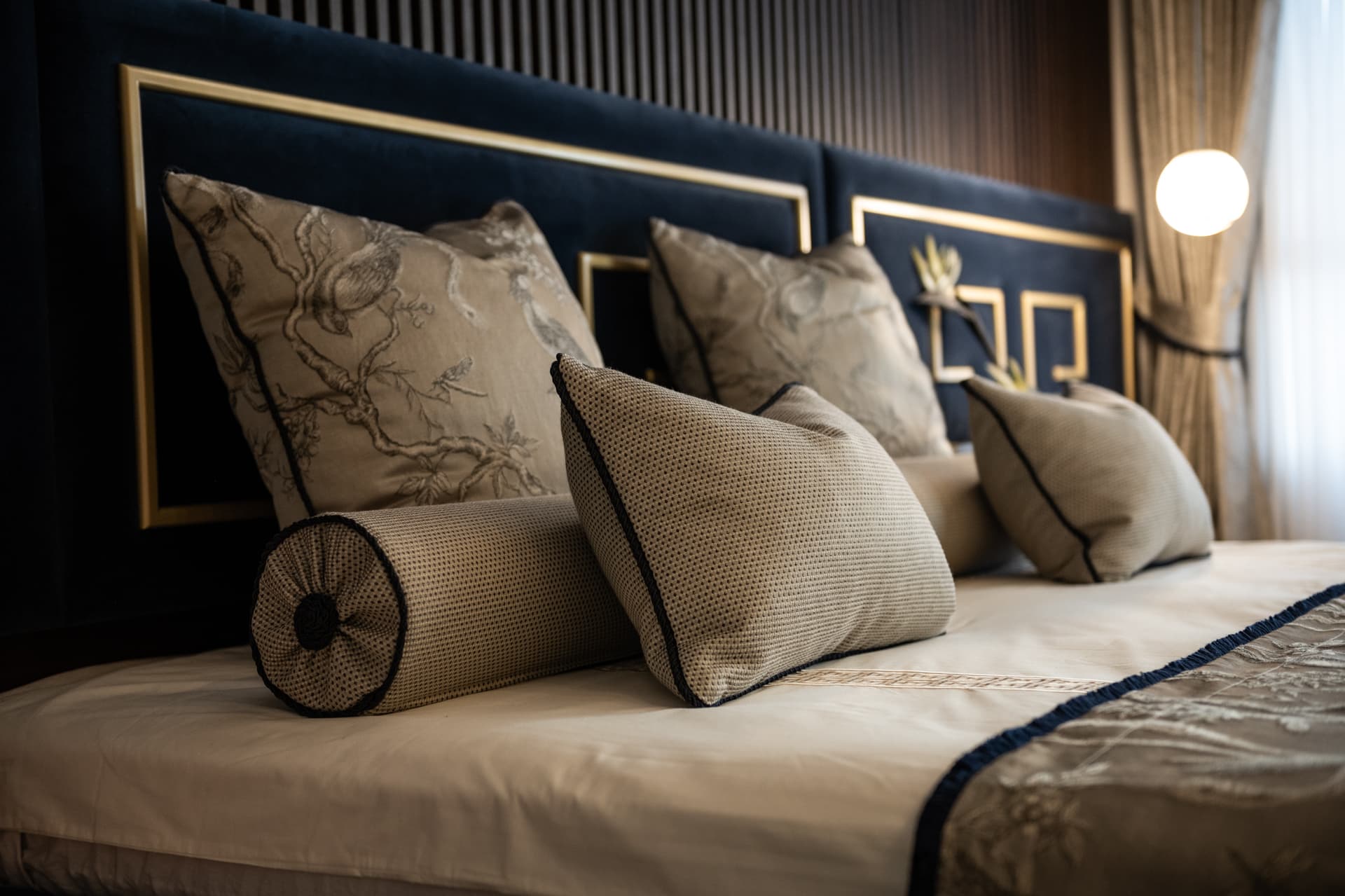 Bird-embroidered cushions and bolsters against a navy velvet headboard with brass fret frames in the master bedroom of Twilight