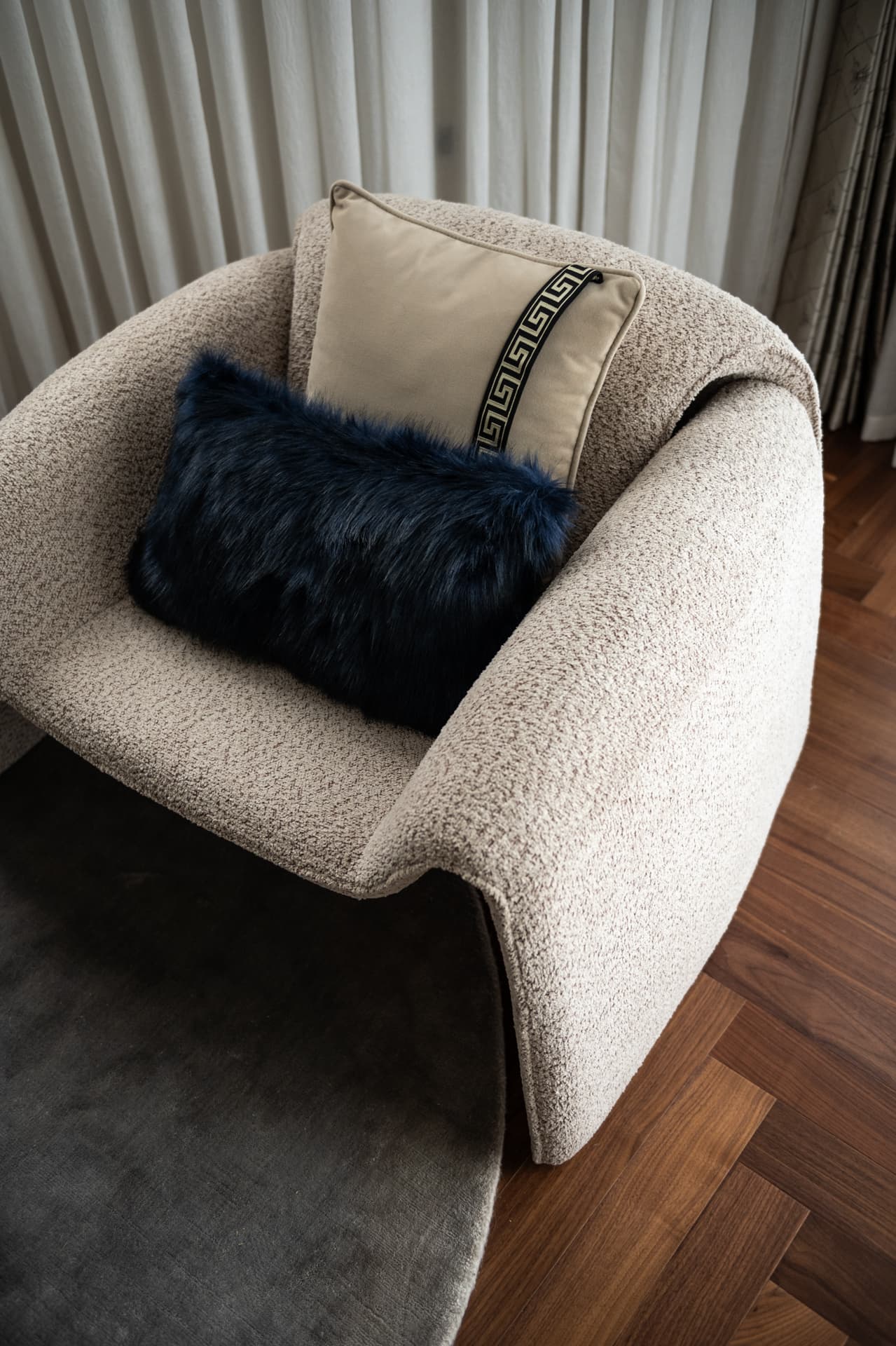 Bouclé tub armchair with a navy faux fur cushion and a Greek key cushion on herringbone wood floor in the master bedroom of Twilight